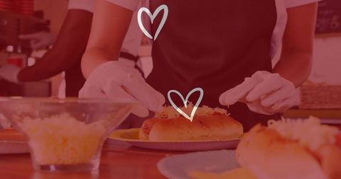 Hands garnishing hotdogs with cheese in professional kitchen