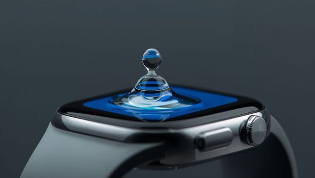 Macro water droplet column on smartwatch screen with reflective metal bezel and crown, blue