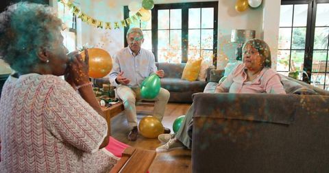 Older adults celebrating home birthday with balloons, confetti, and cozy living room