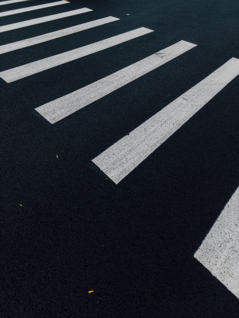 Shows an empty crosswalk on a black asphalt road, usually seen during night or quiet times. Suitable for content about urban planning, road safety, pedestrian regulations, nighttime cityscapes, transportation, and public infrastructure.