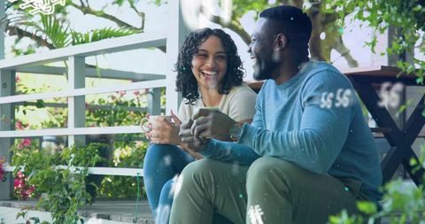 Couple sipping coffee on porch steps sharing warm conversation amid lush garden foliage