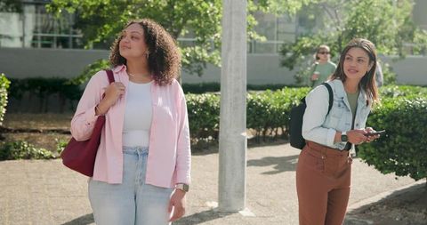 Young Women Walking on Campus Holding Smartphone and Carrying Tote Bag, Urban Commute