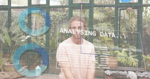 Young man in greenhouse analyzing AR data overlay among tropical plants and glass panels