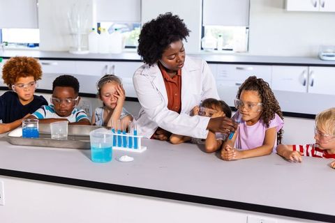 Stem teacher guiding young students through hands-on chemistry experiment with test tubes