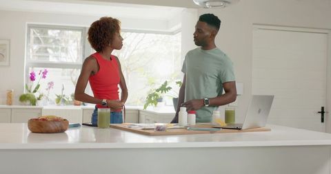 Couple discussing meal plans in bright minimalist kitchen with smoothies and laptop