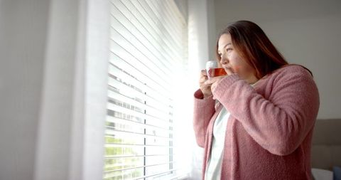 Plus size woman in cozy attire enjoying morning tea by window