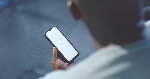 African man holding smartphone with blank screen in waiting area, shallow focus