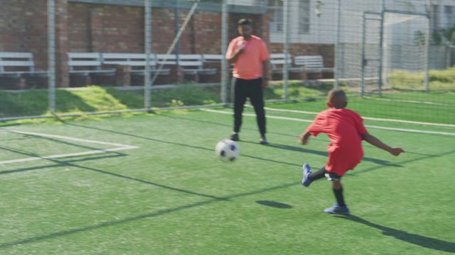 Boys wearing their soccer team uniforms, one taking a shot at goal while playing field shot under bright sunlight. Suitable for sports news, youth sports promotions, athletic clothing ads, teamwork and friendship concepts.