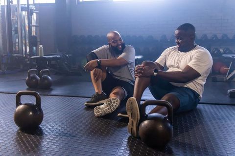 African men resting and laughing after kettlebell training, fitness partners sharing camaraderie