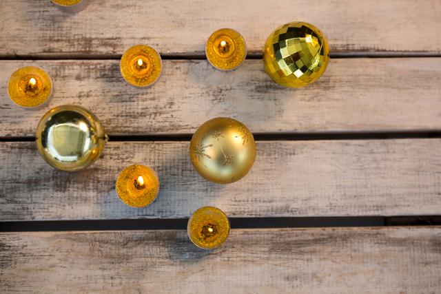 Golden Christmas ornaments and candles arranged on a rustic wooden plank. Ideal for holiday greeting cards, festive invitations, seasonal advertisements, and social media posts celebrating Christmas.