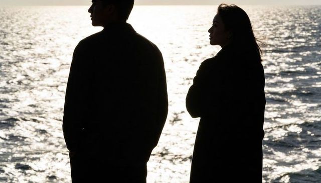 Backlit silhouetted couple standing by sunlit ocean watching horizon at sunset