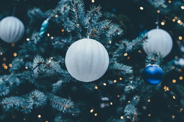 Close-up view of a Christmas tree adorned with white and blue baubles and twinkling lights. Ideal for use in holiday greeting cards, festive advertisements, decorative holiday-themed articles, or social media posts about Christmas celebrations and home decor.