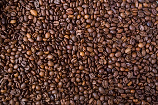 Close-up of a large pile of roasted coffee beans, displaying rich, dark brown hues and textures. Perfect for use in food and drink marketing materials, coffee shop promotions, blogs about coffee culture, or advertisements for coffee-related products.