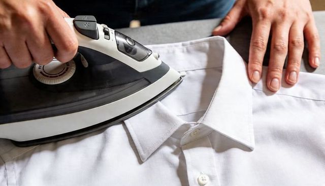 Pressing white dress shirt collar with steam iron closeup hands smoothing fabric