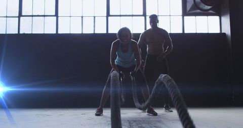 Focused Woman Training with Battle Ropes in Gym