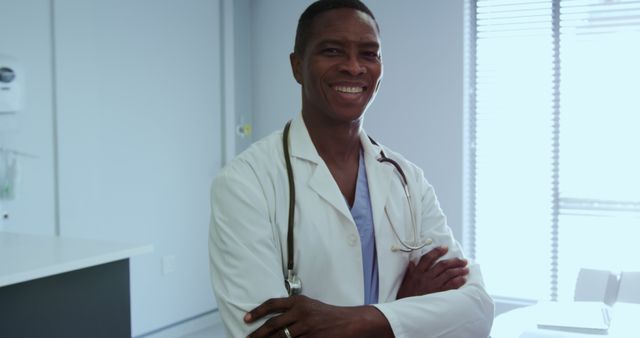 A smiling male doctor in a medical office with a stethoscope hanging around his neck. Suitable for use in healthcare websites, medical advertisements, health blogs, brochures for medical services, and educational materials related to the medical field.