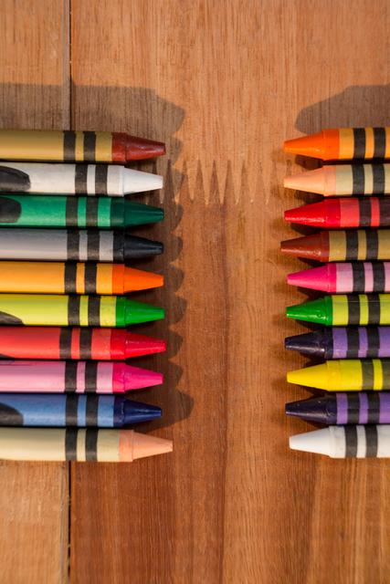 Colorful crayons neatly arranged on a wooden table, showcasing a variety of vibrant hues. Ideal for use in educational materials, art and craft projects, school-related content, and creative advertisements. Perfect for illustrating themes of creativity, learning, and childhood.