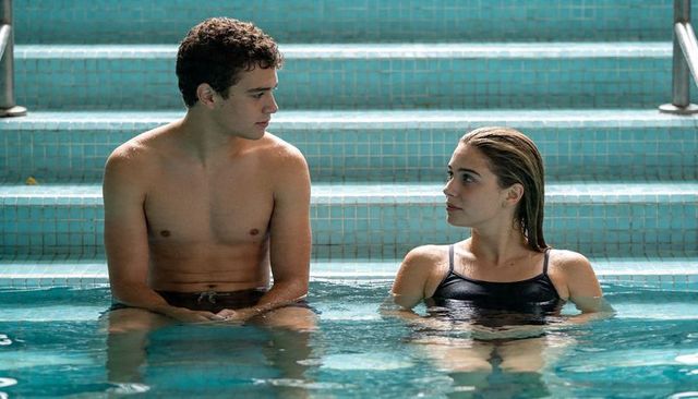 Teenagers talking on pool steps, shirtless young man and woman in black swimsuit