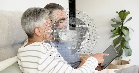 Mature couple sitting on sofa using tablet with holographic globe overlay