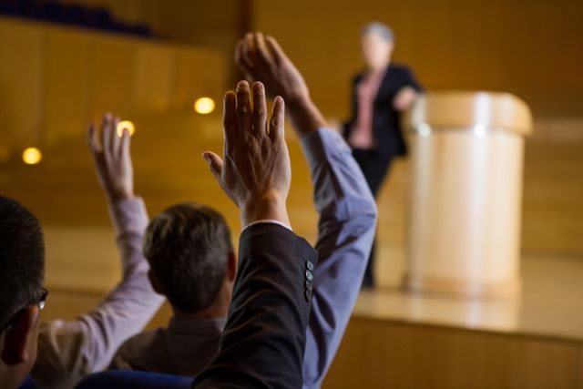 Business executives actively participating in a conference by raising their hands. Ideal for use in corporate training materials, business presentations, and articles on professional development and engagement.