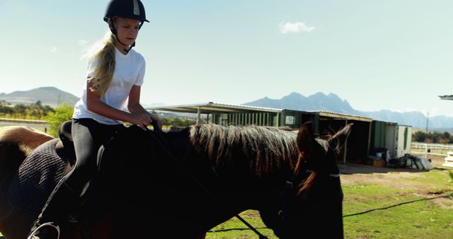 A young Caucasian girl is horseback riding in an outdoor setting, with copy space. She is focused on her equestrian practice, demonstrating the bond and cooperation between rider and horse.