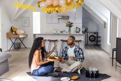 Diverse couple celebrating anniversary with loft kitchen picnic, balloons and champagne