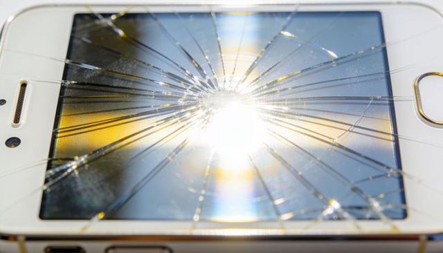 White smartphone displaying shattered front glass with bright central glare and gold home button