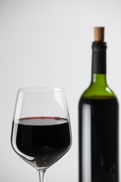Bottle and a glass of red wine against white background