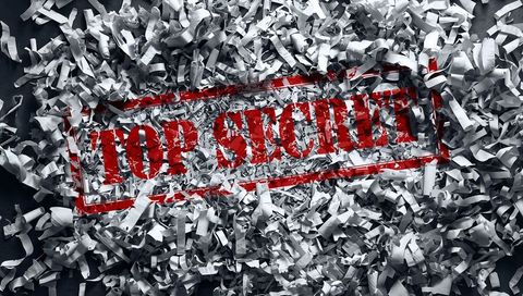 Top secret stamp lying on shredded paper with red ink smears