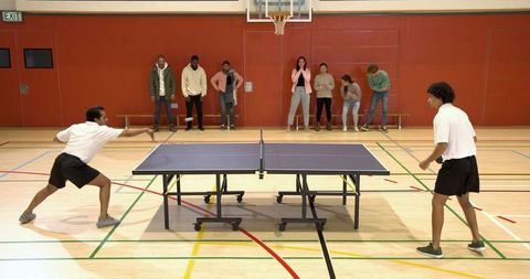 Friends Playing Table Tennis in Sports Hall with Basketball Hoop