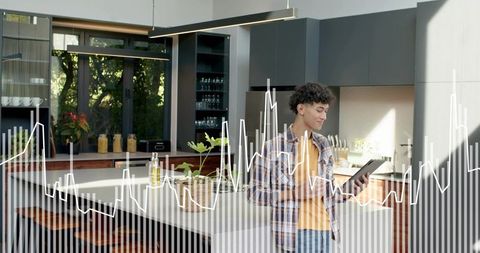 Young man tapping tablet at modern kitchen island with data chart overlay and sunlight