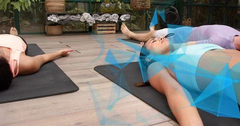Group practicing restorative yoga outdoors on wooden deck with black mats and greenery