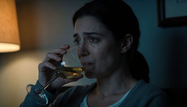 Woman sipping wine on sofa at night, holding glass, contemplative moody moment