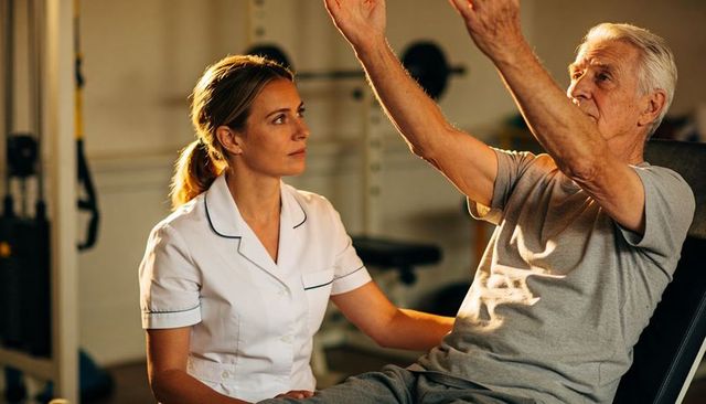 Assisting senior with arm exercises in rehabilitation gym — therapist guiding movement