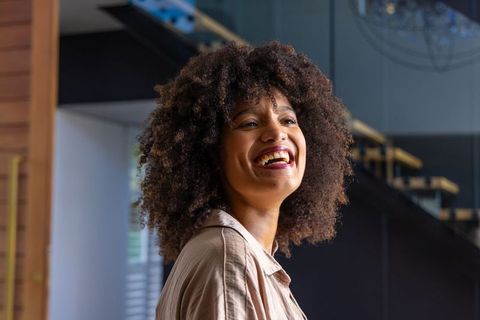 Smiling african american woman looking up in modern sunlit foyer with wooden staircase