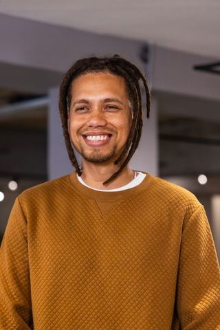 African american man smiling and standing in modern interior wearing mustard pullover