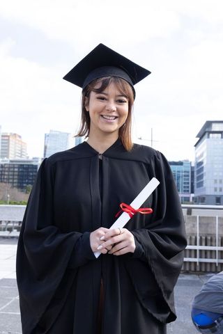 Smiling graduate holding diploma on urban rooftop with city skyline background