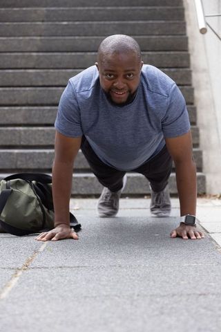 Adult african man doing push-ups on urban steps wearing smartwatch and athletic gear