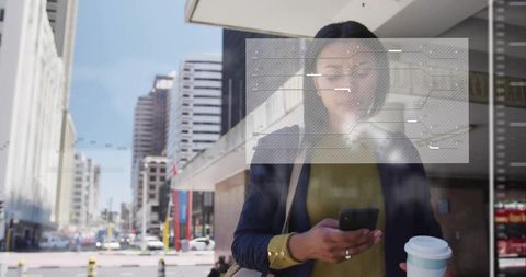 Urban professional checking phone at reflective glass holding coffee and tote bag during commute