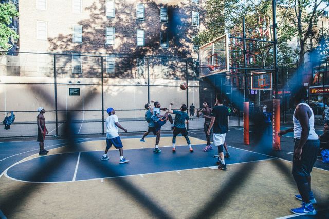 People playing basketball on an outdoor city court. Perfect for themes related to urban life, fitness activities, sports, teamwork, energy, and community engagement. Useful for illustrating lively urban environments, depicting recreational activities, and promoting sports programs.