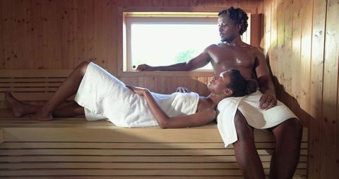 Couple relaxing in wooden sauna wrapped in towels sharing intimate spa moment