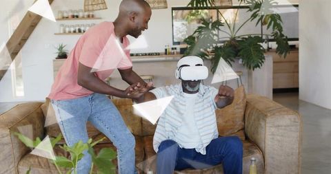 Senior man wearing VR headset reaching and pointing while son steadying arm on sofa