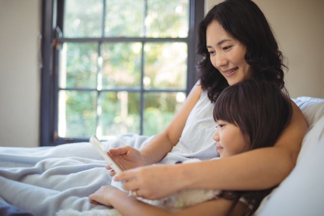 Mother and daughter using digital tablet on bed in bed room at home