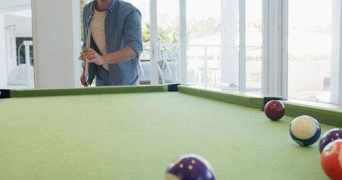 Player aiming cue on sunlit green pool table in modern game room with daylight streaming