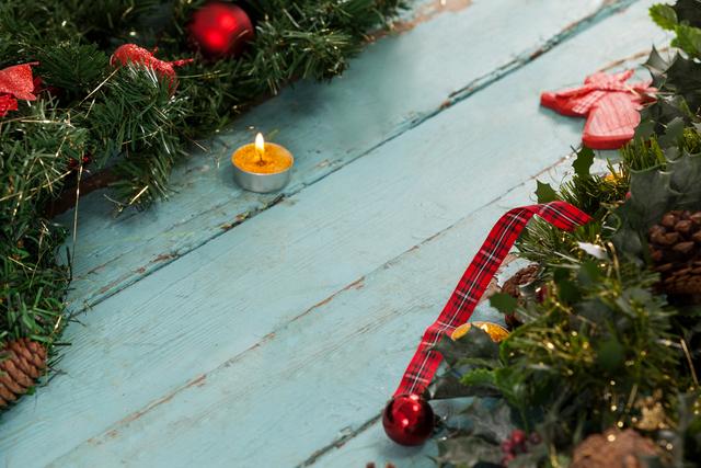 Christmas decorations arranged around a tealight candle on a wooden plank surface. Ideal for holiday-themed projects, greeting cards, festive advertisements, or seasonal social media posts.