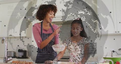 Mom teaching daughter baking with whisk and eggs in modern kitchen, dotted globe overlay