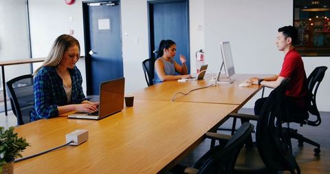 Business team collaborating at large work table using laptops