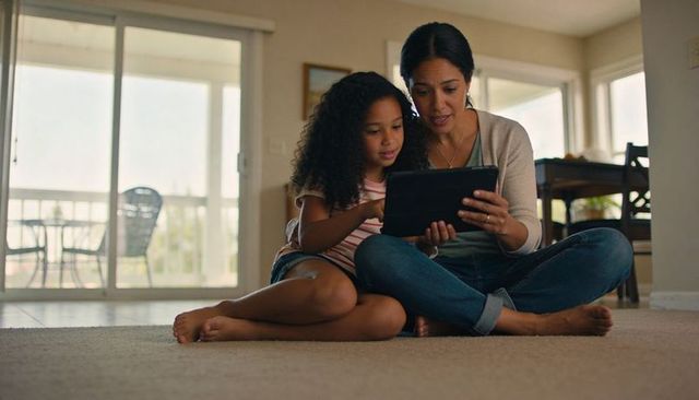 Mother and daughter sharing tablet on living room floor, cozy bonding and learning moment