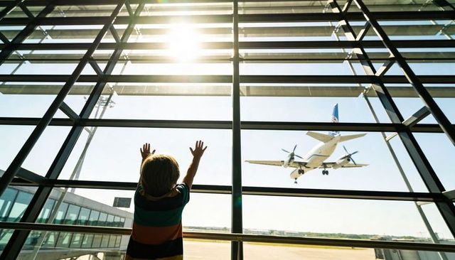 Child Reaching Toward Landing Twin-Prop Plane Through Glass at Bright Airport Terminal