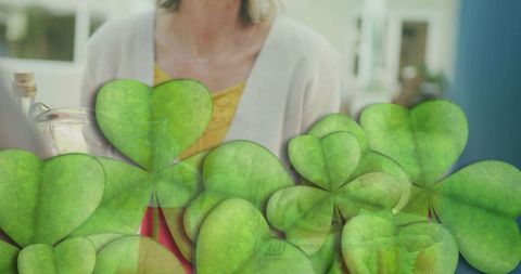 Mature blonde woman touching necklace adjusting to sunlight at window with clover leaves
